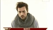 a man wearing a scarf and a sweater is standing in front of a banner that says marco .