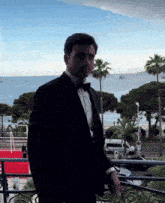 a man in a tuxedo standing on a balcony overlooking the ocean