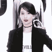a woman wearing a choker and a black jacket is standing in front of a white wall .