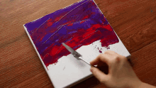 a person is using a spatula to spread purple and red paint on a canvas