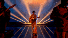 a man playing an acoustic guitar on a stage with other men playing guitars