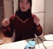 a woman in a red sweater is sitting at a table with a phone on it
