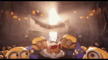 a group of minions are standing in front of a stage with a light coming out of the top .