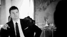 a man in a suit and tie is sitting in a chair with his hands on his hips .