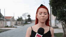 a woman with red hair and a tattoo of a heart on her shoulder holds a microphone