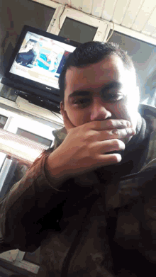 a man covering his mouth with his hand in front of a flat screen tv