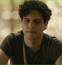 a man with curly hair is wearing a black t-shirt and looking at the camera .