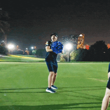 a man is holding a blue pom pom on a golf course at night