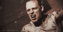 a man with a lot of tattoos on his arms and chest is screaming in a dark room .