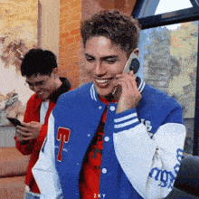 a man wearing a blue jacket with the letter t on it talks on a cell phone
