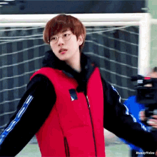 a young man wearing glasses and a red vest is standing in front of a goal
