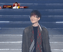 a man wearing glasses and a jacket stands in front of a screen that says ao139
