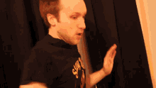 a man wearing a black shirt with the word now on it making a funny face