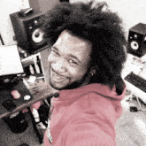 a man in a red hoodie is smiling in front of a computer and speakers