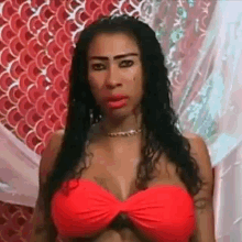 a woman in a red bikini top is standing in front of a fish scale patterned wall .