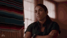 a woman is sitting in a room with her arms crossed and looking at the camera .