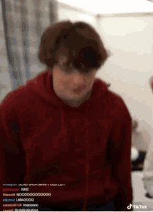 a man in a red hoodie is standing in a room and looking at the camera .