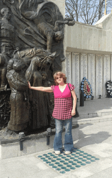 a woman in a pink plaid shirt stands in front of a statue of people
