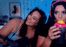 two women are sitting in front of a microphone and one is drinking from a pink container
