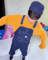 a young boy wearing overalls and a yellow sweater is dancing