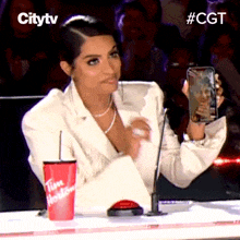a woman sitting in front of a microphone holding a cell phone and a tim hortons cup in front of her