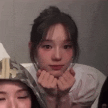 a girl is making a heart shape with her hands while sitting next to another girl .