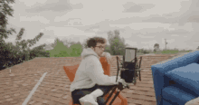 a man is sitting on a chair on top of a roof with a microphone in front of him .