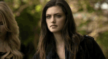 a woman in a black jacket is standing next to another woman in a forest .