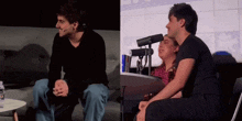 a man sitting on a couch next to a woman sitting at a table with microphones