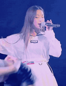 a woman singing into a microphone wearing a white shirt that says bsdd