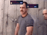 a man with a mustache is standing in front of a wooden wall