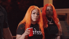 a woman with orange hair is holding a red cup and wearing a shirt that says atss