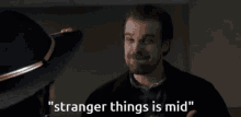 a man is talking to another man in a dark room and the words `` stranger things is mid '' are visible .