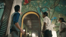 a man and a woman are standing in front of a mirror in a room with a mural on the wall