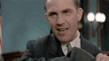 a man in a suit and tie is smiling while holding a piece of clothing .