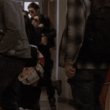 a group of people are walking down a hallway including a man wearing a brown jacket