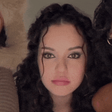 a woman with curly hair looks at the camera with a serious look on her face
