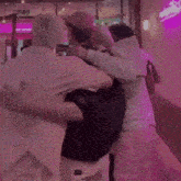 a group of people are hugging each other in a room with a pink light behind them .