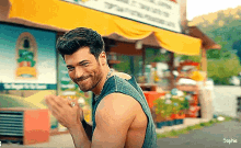 a man without a shirt is smiling in front of a store with a yellow awning .
