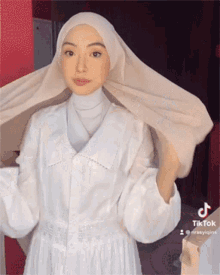 a woman wearing a white dress and a white hijab has tiktok written on the bottom