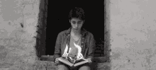 a young boy is sitting on a window sill reading a book that is on fire .