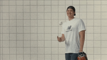 a man wearing a new balance t-shirt laughs while holding a baseball
