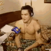 a shirtless man wearing headphones is sitting on a bed with a microphone .