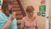 two women are standing next to each other in front of a fire exit sign