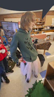 a boy in a green hoodie is standing in front of a computer screen that says ' how to build a robot ' on it