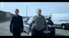 two men standing next to a car with the license plate number 208 531