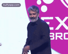 a man with a beard is standing on a stage in front of a pink and white logo .