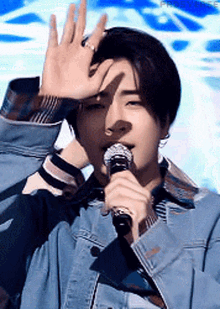 a young man in a denim jacket is singing into a microphone and making a hand gesture