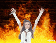 a woman in a white dress is holding a microphone in front of a fire background