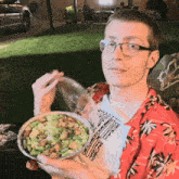 a man wearing a hawaiian shirt is eating a salad outside